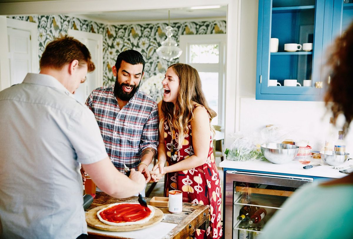 Smejúci sa pár pripravuje pizzu spolu s priateľmi v kuchyni