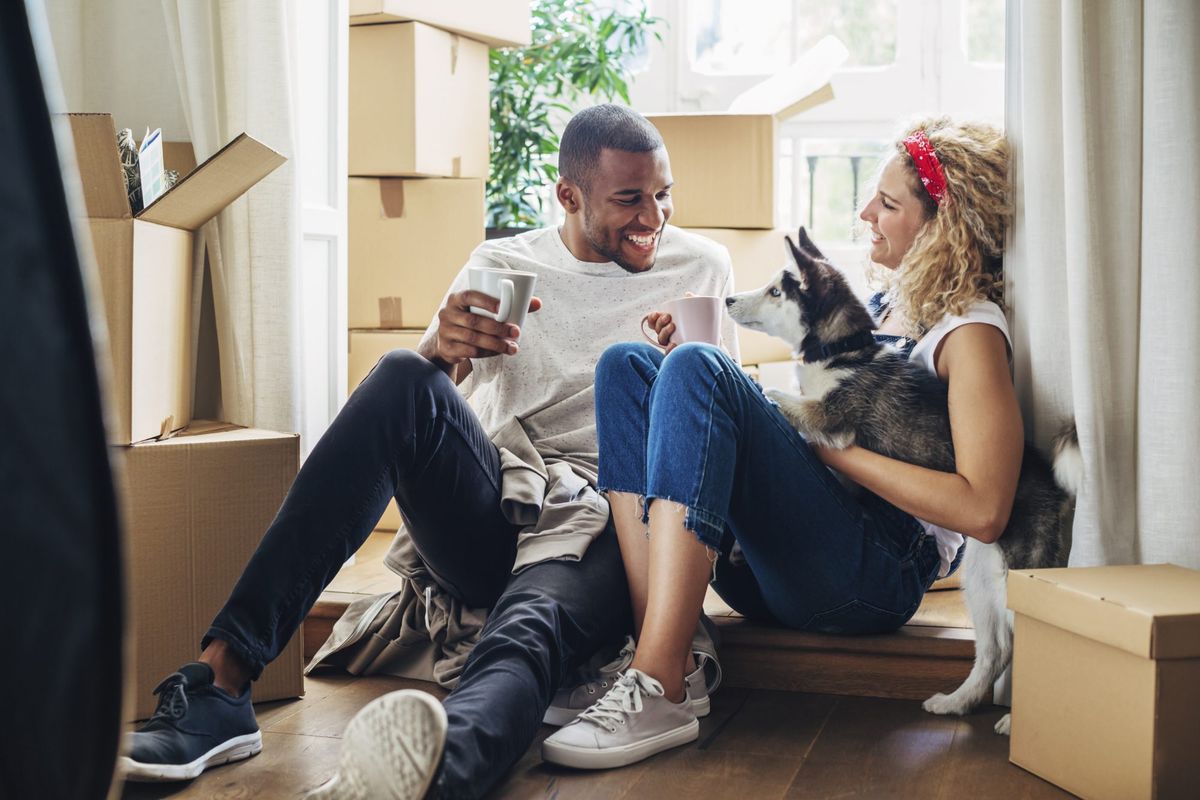 Srečen par se igra s psom, medtem ko sedi na vratih v novi hiši
