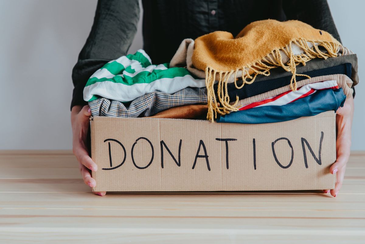 Ženska ima kartonsko škatlo za donacije, polno zloženih oblačil